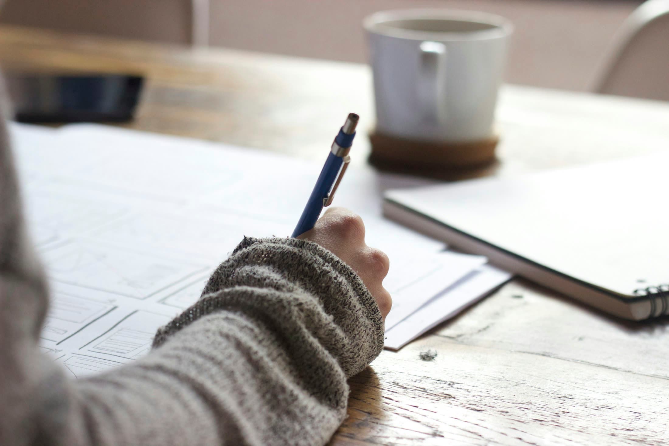 Someone in a cosy jumper writing notes beside a coffee