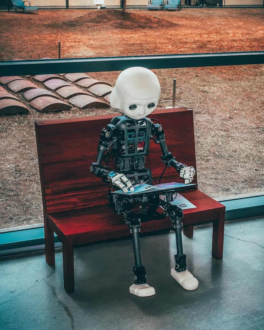 A small robot reading a book on a bench